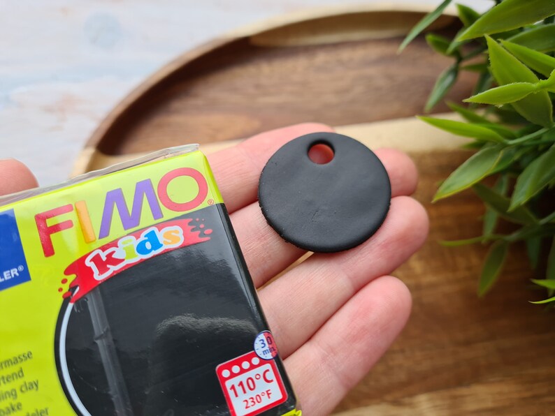 May include: A black FIMO Kids modelling clay package with the text "FIMO Kids" and "110&deg;C 230&deg;F" on the front. A black clay circle with a hole in the centre is shown in the background.