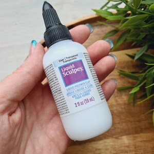 May include: A clear bottle of Liquid Sculpey liquid polymer clay. The bottle is labeled with the brand name and product information, including the size: 2 fl oz (59 ml).