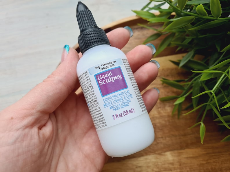 May include: A clear bottle of Liquid Sculpey liquid polymer clay. The bottle is labeled with the brand name and product information, including the size: 2 fl oz (59 ml).