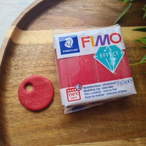 May include: A red FIMO Effect modeling clay stick with a diamond-shaped logo and the text "FIMO EFFECT". The package also includes the text "Modelliermasse ofenhärtend 57 g (2 oz) e" and "110°C 230°F".