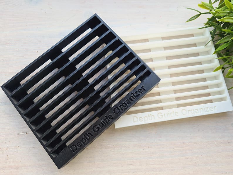 Peut inclure: Deux organisateurs rectangulaires &agrave; fentes, l'un noir et l'autre blanc. Le texte "Depth Guide Organizer" est imprim&eacute; sur les deux. Ces organisateurs sont con&ccedil;us pour ranger et organiser des objets.