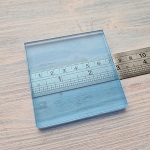May include: A clear blue glass square with a ruler measuring 7 inches across the top. The ruler is marked in 1/32 inch increments.
