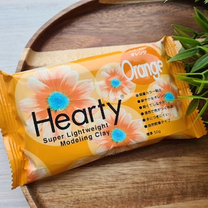 Peut inclure: Un paquet d'argile à modeler Hearty Super Lightweight de couleur orange. L'emballage présente un motif floral et le texte "Orange" en japonais et en anglais.