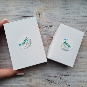 May include: Two white rectangular boxes with rounded corners, one larger than the other, are displayed. Each box has a circular sticker with the text "Polymer Clay" and a website address. The boxes are on a light wood surface.