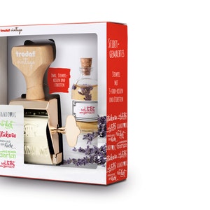 K&ouml;nnte beinhalten: Ein goldfarbener Stempel mit einem Holzgriff und eine klare Glasflasche mit einem Korkverschluss. Der Stempel hat ein wei&szlig;es Etikett mit dem Text "HANDMADE" und "LIEBE" in Rot. Die Flasche hat ein wei&szlig;es Etikett mit dem Text "LIEBE" und "gemacht". Der Hintergrund ist wei&szlig;.