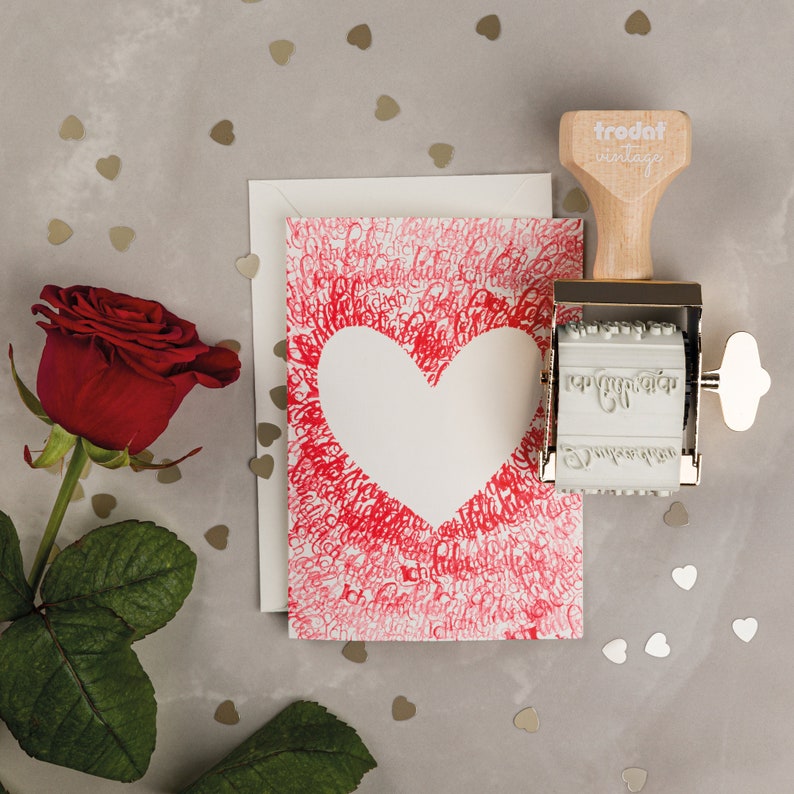 Puede incluir: Una tarjeta de San Valent&iacute;n roja y blanca con una forma de coraz&oacute;n en el centro. La tarjeta est&aacute; rodeada de un patr&oacute;n de corazones rojos y las palabras "Te amo". Tambi&eacute;n se ve un sello de goma de estilo vintage con las palabras "trodat vintage" en la imagen.