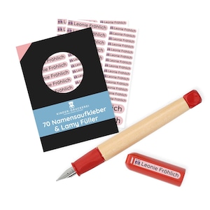 May include: A set of 70 pink and white name labels with the text "Leonie Fröhlich" printed on them. The labels are packaged with a wooden pen with a red cap and a red nib. The packaging is black with a blue and white label that says "KINDER-DRUCKEREI 70 Namensaufkleber & Lamy Füller".