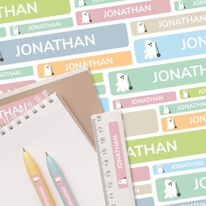 Puede incluir: Un conjunto de etiquetas rectangulares de colores con un gráfico de fantasma y el nombre "Jonathan" impreso en ellas. Las etiquetas están diseñadas para útiles escolares y artículos personales.