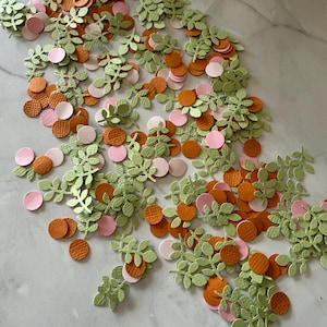 Peut inclure: Un assortiment de découpes de papier de différentes formes et couleurs. L'image présente des formes de feuilles vert clair, ainsi que des cercles orange et roses. Les découpes sont dispersées sur une surface claire, créant un arrangement décoratif.