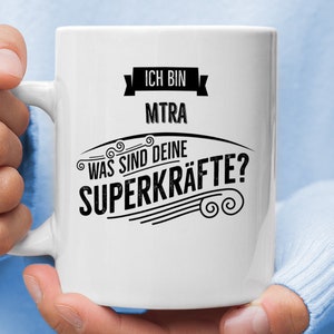 Könnte beinhalten: Weiße Keramiktasse mit schwarzem Text, der "Ich bin MTRA Was sind deine Superkräfte?" lautet.