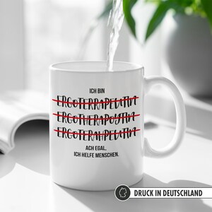 May include: White ceramic mug with black text that reads "ICH BIN" with three lines of text crossed out that read "ERGOFERRAPELATIVT", "ERGOTHERAPOYTAH", and "ERGOFERAMPELATINA". The text below the crossed out lines reads "ACH EGAL, ICH HELFE MENSCHEN."
