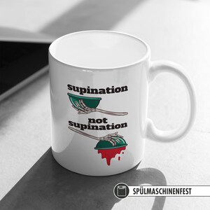 May include: White ceramic coffee mug with a black and green illustration of a skeleton hand holding a bowl. The text "supination" and "not supination" is printed on the mug.