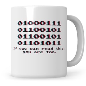 Könnte beinhalten: Eine weiße Keramiktasse mit einem schwarzen und roten Binärcode-Design, das "01000111 01100101 01100101 01101011" lautet und den Text "Wenn du das lesen kannst, bist du es auch."