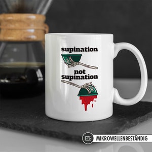 May include: White ceramic mug featuring a black and green illustration of a skeleton hand holding a bowl. The text "supination" and "not supination" is printed on the mug. The mug is microwave safe.