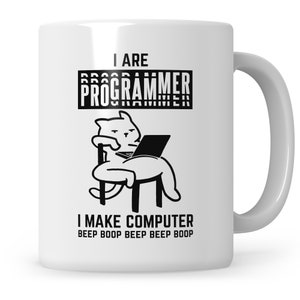 Könnte beinhalten: Eine weiße Keramiktasse mit einer Schwarzweißillustration einer Katze, die auf einem Stuhl sitzt und einen Laptop benutzt. Der Text "I ARE PROGRAMMER I MAKE COMPUTER BEEP BOOP BEEP BEEP BOOP" ist auf die Tasse gedruckt.