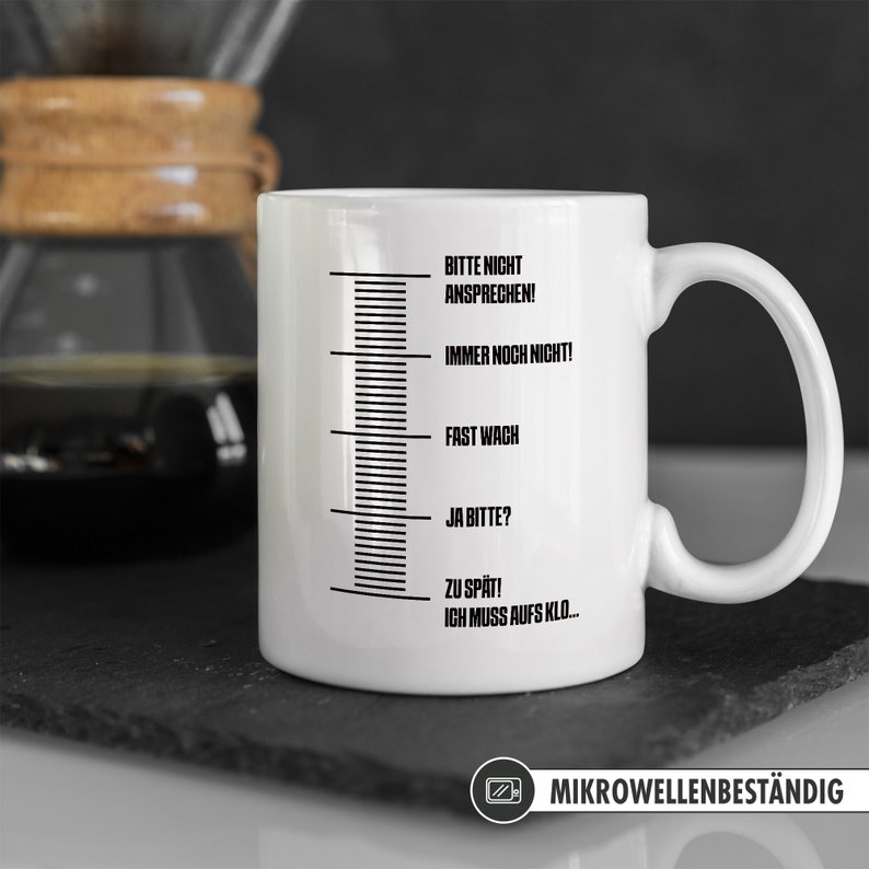 May include: White ceramic coffee mug with a black scale and text that reads "Bitte nicht ansprechen! Immer noch nicht! Fast wach Ja bitte? Zu sp&auml;t! Ich muss aufs Klo..."  The mug is microwave safe and has a black and white image of a microwave.