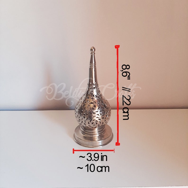 May include: Silver metal decorative lamp with a cut-out design. The lamp is 8.6 inches tall and 3.9 inches wide.