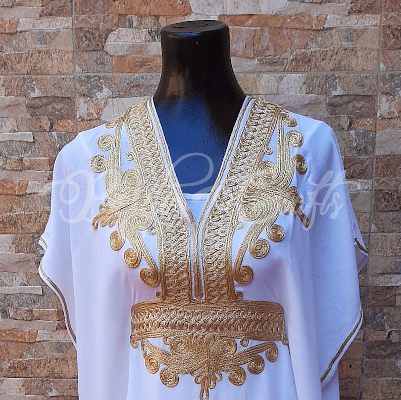 May include: White kaftan with gold embroidery. The embroidery features intricate floral and geometric patterns.