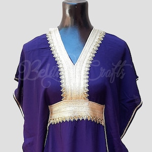 May include: A purple kaftan with gold trim around the neckline and waist. The kaftan has a V-neck and long sleeves.
