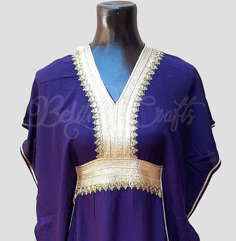 May include: A purple kaftan with gold trim around the neckline and waist. The kaftan has a V-neck and long sleeves.