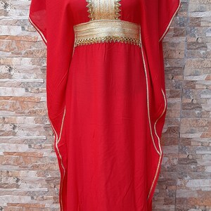 Może przedstawiać: Czerwona kaftan z haftem i ozdobami w kolorze złotym. Kaftan ma dekolt w kształcie litery V i pasek w talii.