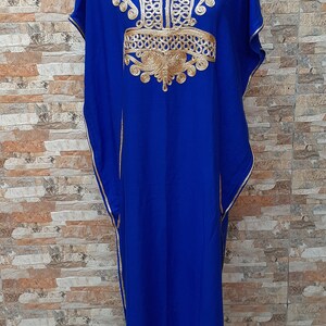 May include: A royal blue kaftan with gold embroidery. The kaftan has a V-neckline and short sleeves. The embroidery is intricate and features a floral design.