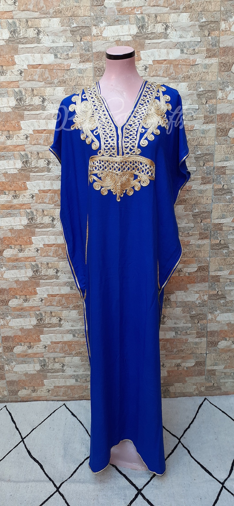 May include: A royal blue kaftan with gold embroidery. The kaftan has a V-neckline and short sleeves. The embroidery is intricate and features a floral design.