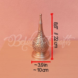 May include: A gold metal candle holder with a decorative, intricate design. It is 8.6 inches tall and 3.9 inches wide.