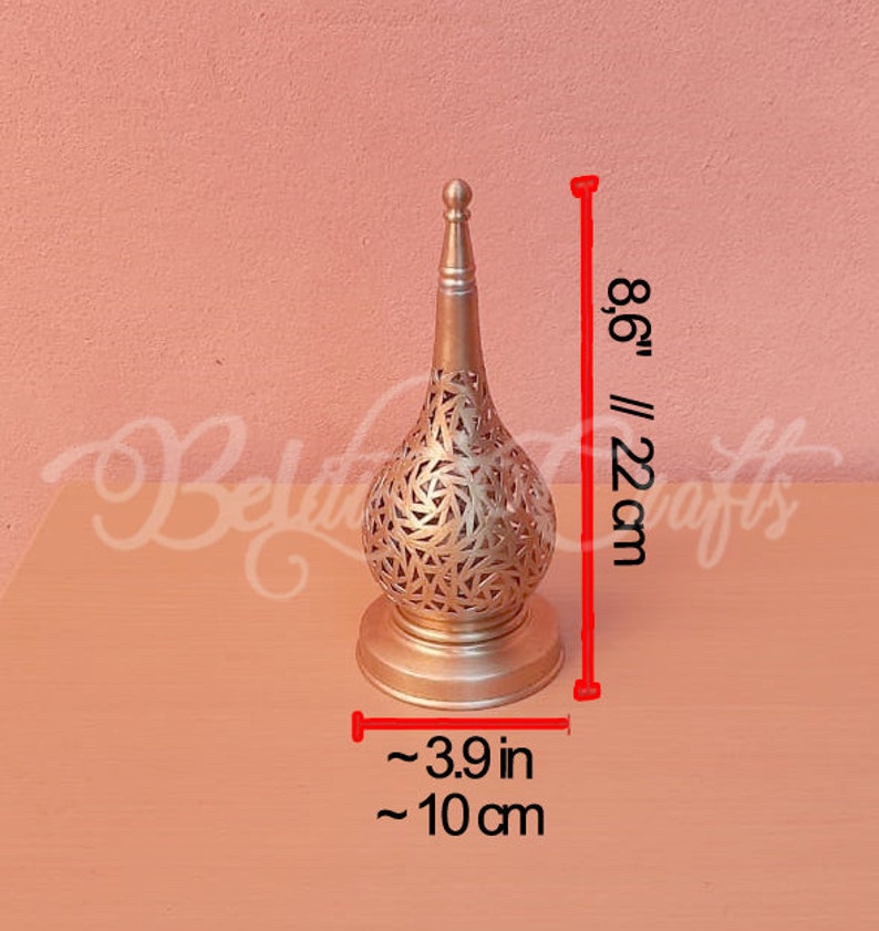 May include: A gold metal candle holder with a decorative, intricate design. It is 8.6 inches tall and 3.9 inches wide.