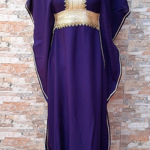 May include: A long, flowing purple kaftan with gold trim and embroidery. The kaftan has a V-neckline and a belt at the waist.