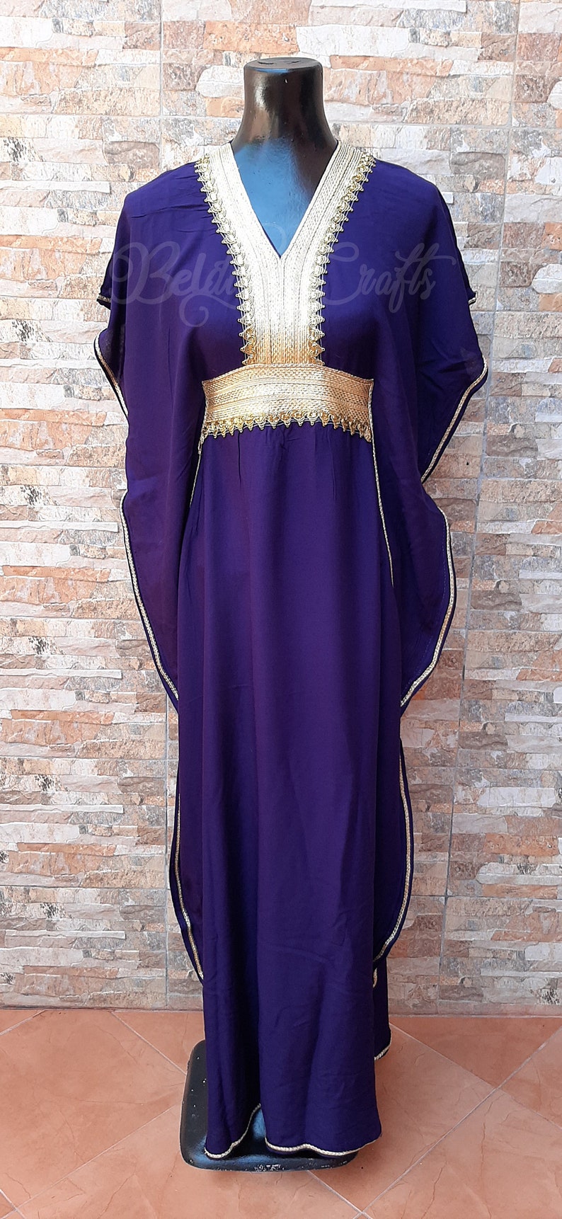 May include: A long, flowing purple kaftan with gold trim and embroidery. The kaftan has a V-neckline and a belt at the waist.