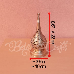Puede incluir: Una l&aacute;mpara decorativa de metal dorado con un dise&ntilde;o redondo y calado. La l&aacute;mpara mide 22 cm de alto y 10 cm de ancho.