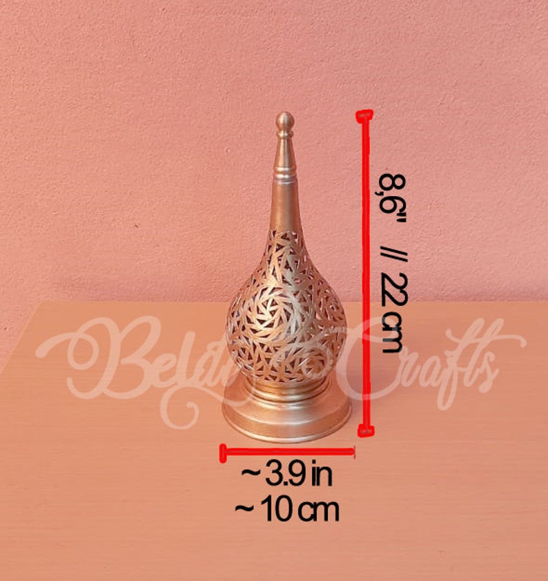 Puede incluir: Una l&aacute;mpara decorativa de metal dorado con un dise&ntilde;o redondo y calado. La l&aacute;mpara mide 22 cm de alto y 10 cm de ancho.