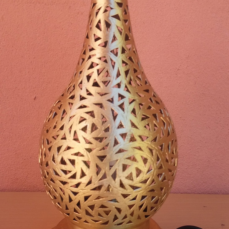 Puede incluir: Una l&aacute;mpara de metal de color dorado con un patr&oacute;n geom&eacute;trico decorativo, intrincado y delicado. La l&aacute;mpara tiene la forma de una l&aacute;grima.