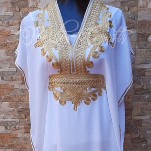 May include: A white kaftan with gold embroidery. The embroidery is in a floral pattern and is around the neckline and the waist.