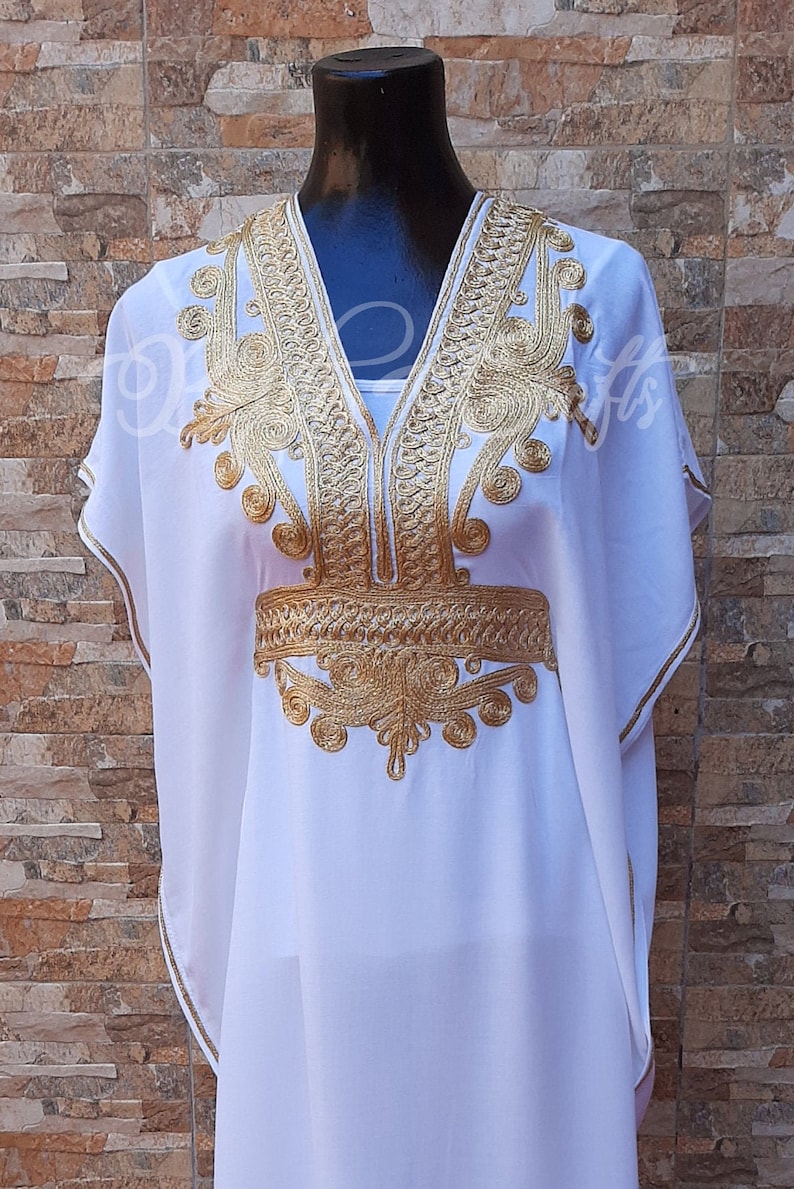 May include: A white kaftan with gold embroidery. The embroidery is in a floral pattern and is around the neckline and the waist.
