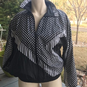 May include: Black and white windbreaker jacket with a polka dot and striped pattern. The jacket has a zipper closure and long sleeves.