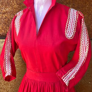 May include: A red dress with white and gold lace trim on the sleeves and shoulders. The dress has a fitted bodice and a full skirt.