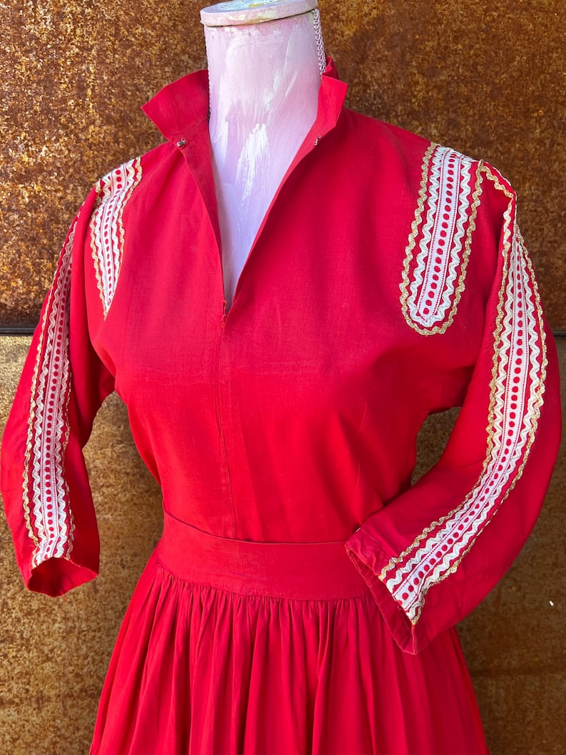 May include: A red dress with white and gold lace trim on the sleeves and shoulders. The dress has a fitted bodice and a full skirt.