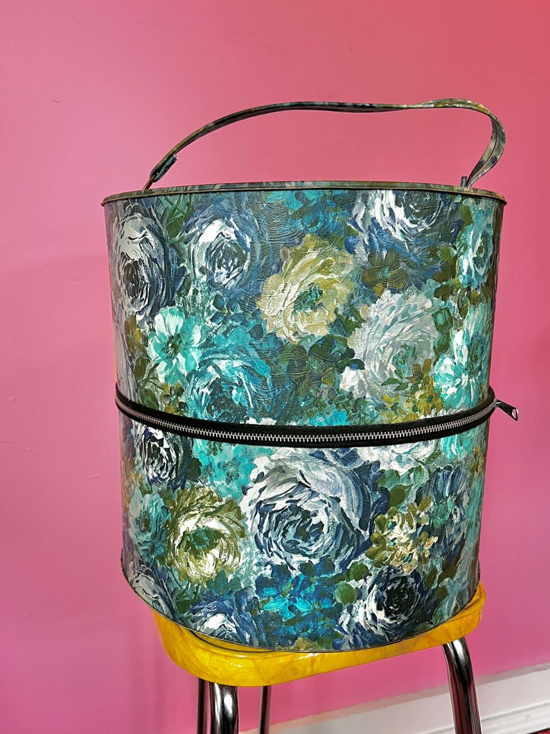 May include: A vintage hat box with a floral pattern in shades of blue, green, and white. The box has a zipper closure and a handle.