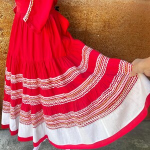 May include: A red dress with white and gold embroidery. The dress has a tiered skirt and a fitted bodice. The dress is made of a lightweight fabric and is perfect for a summer party.