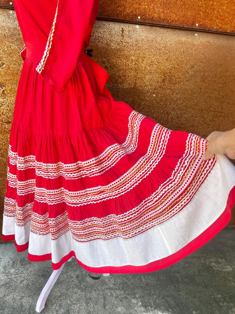 May include: A red dress with white and gold embroidery. The dress has a tiered skirt and a fitted bodice. The dress is made of a lightweight fabric and is perfect for a summer party.