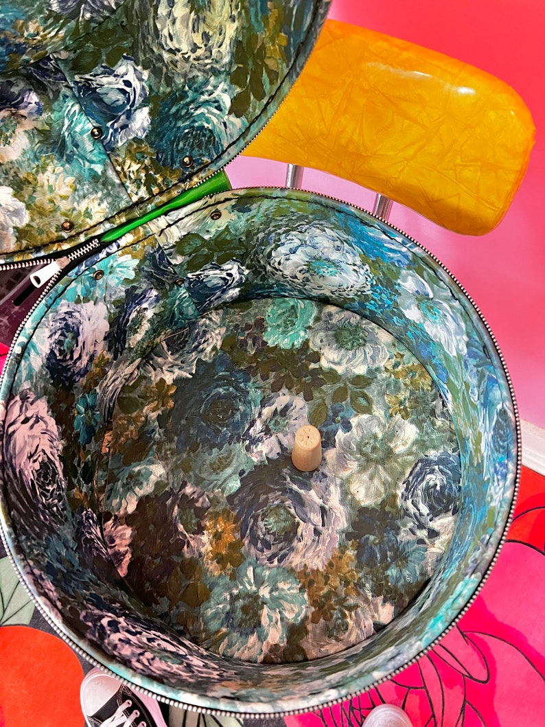 May include: A vintage floral patterned hat box with a green lining and a cork stopper in the center. The box is open and the inside is visible.