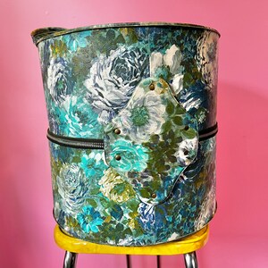 May include: A vintage floral patterned hat box with a zipper closure and a metal accent on the side. The hat box is sitting on a yellow stool.