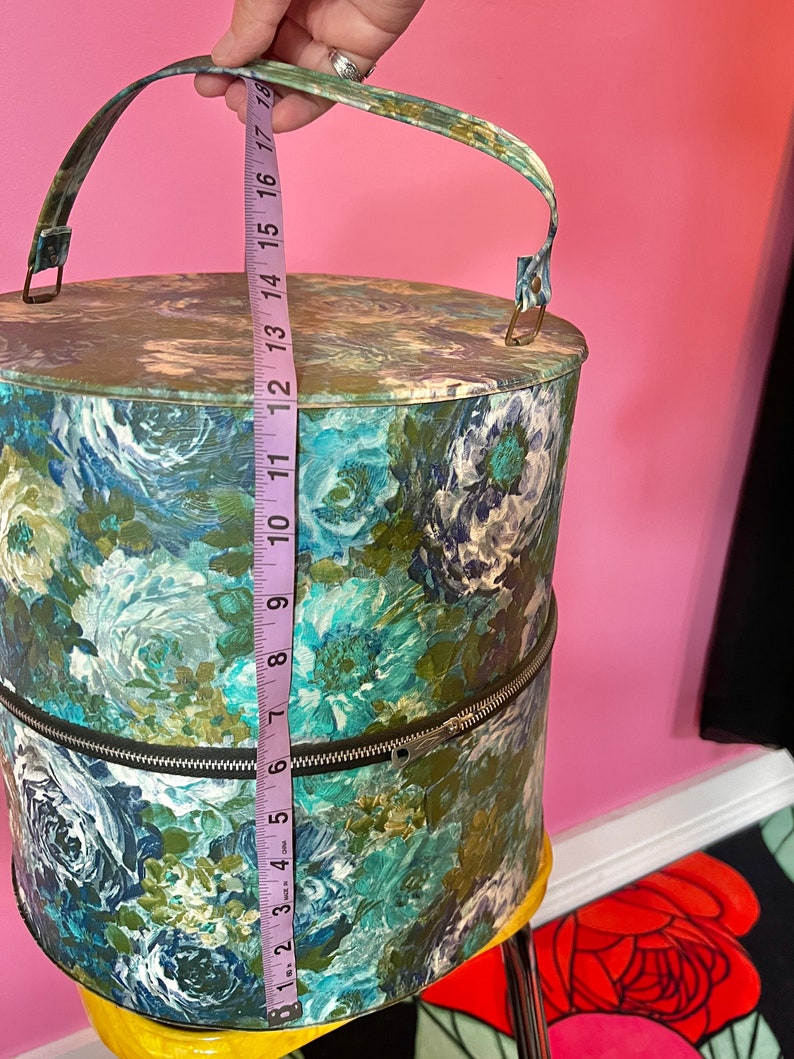 May include: A vintage hat box with a floral print in shades of blue, green, and white. The box has a zipper closure and a handle. The box is 17 inches tall.