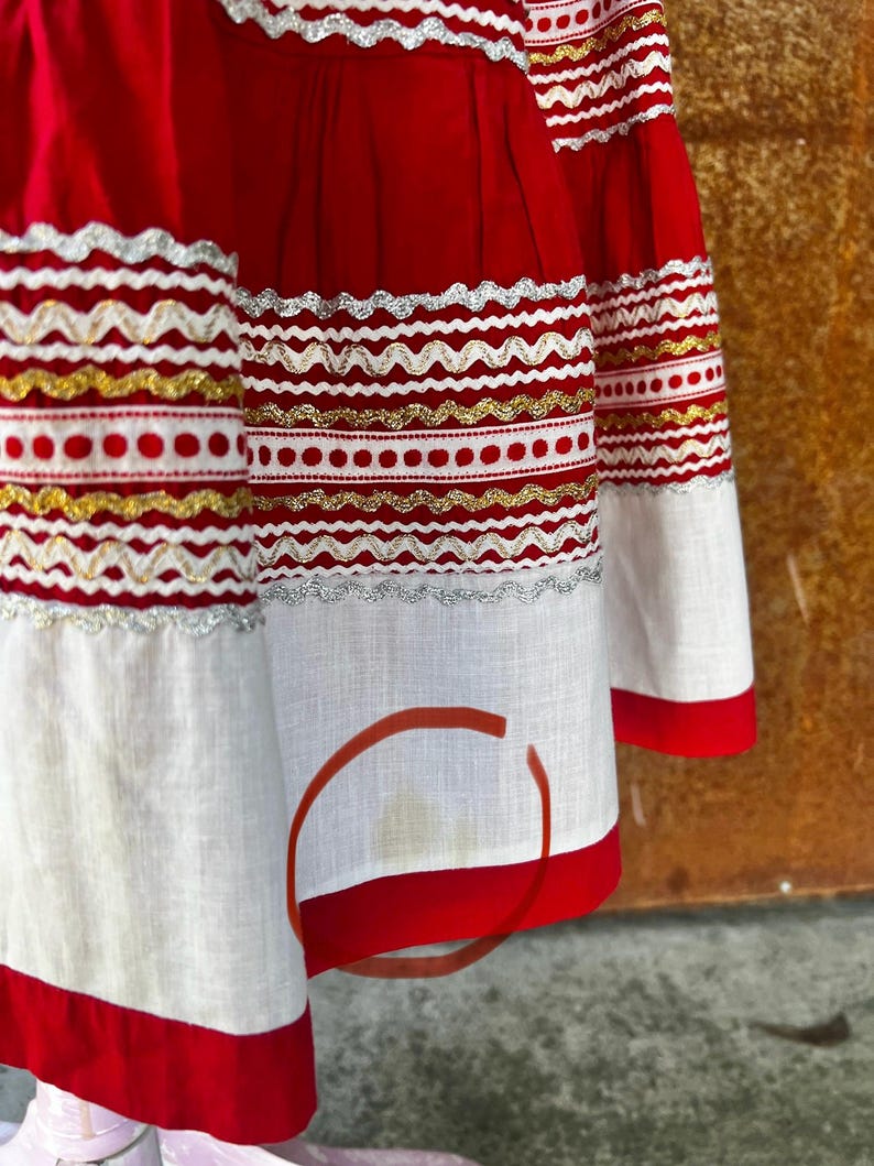 May include: A red skirt with white and gold trim. The skirt has a white cotton lining and a red waistband. The skirt is made of a lightweight fabric and has a gathered design.
