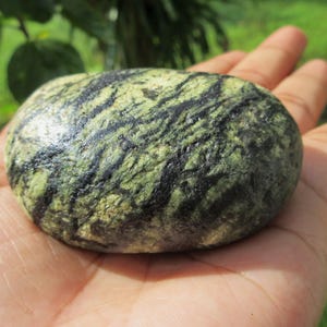 May include: A smooth, green and black stone with a swirling pattern. The stone is being held in a hand.