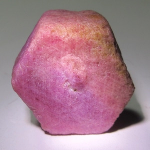 May include: A large, pink, hexagonal ruby crystal with a rough, natural surface.