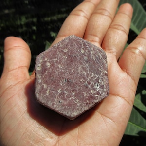 Puede incluir: Un gran cristal de rubí hexagonal rojo oscuro con una superficie rugosa y texturizada.