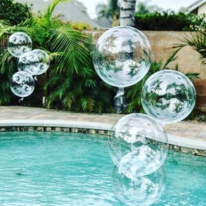 May include: Clear bubble balloons floating in a swimming pool. The balloons are reflecting the surrounding trees and sky.
